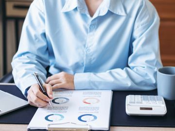 Person analyzing charts and data with a pen at a desk.