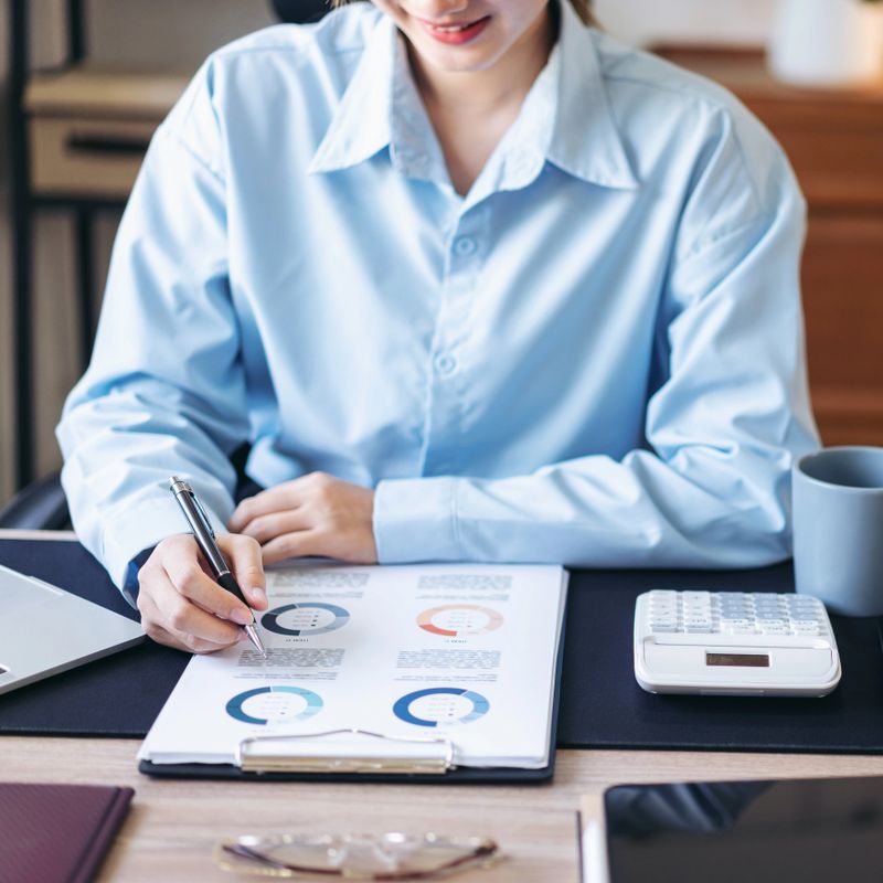 Businesswoman is reading information of new business project and taking notes in document while thoughtful about accounting of business and working on laptop at modern office.