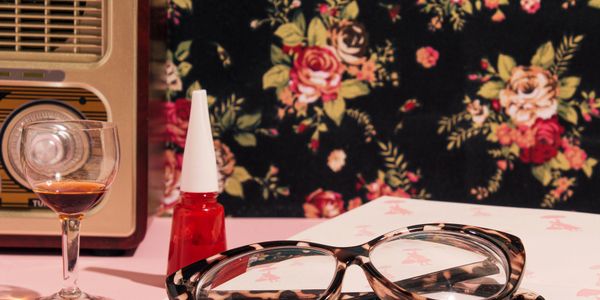 Vintage glasses, red nail polish, and a glass of wine on a floral table.