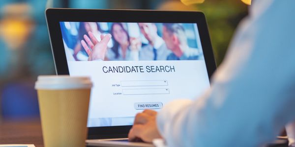 Person using a laptop to search for job candidates online with a coffee cup nearby.