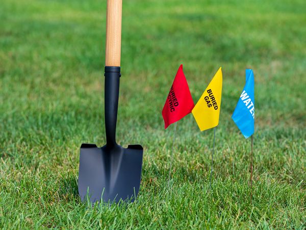 Shovel next to buried utility flags on grassy ground.