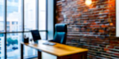 Modern office with wooden desk, black chair, and large windows.