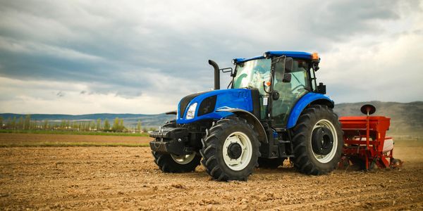 A blue tractor working on a plowed field under a cloudy sky.