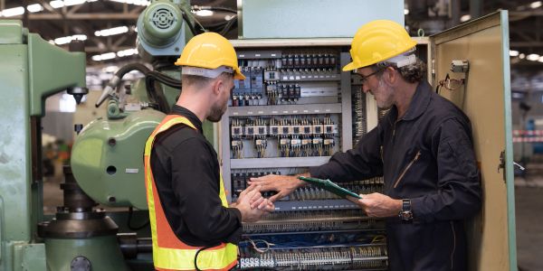 Two engineers examining electrical panel in factory.