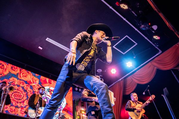 A vibrant, low-angle photograph capturing a male singer intensely performing on stage with his band.