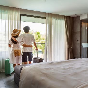 Pareja en habitación de hotel con maletas junto a la ventana.