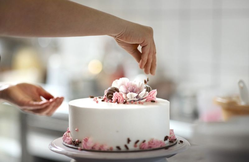 Closeup of an unrecognizable woman decorating a cake at a small family owned cake shop.
