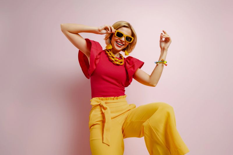 Playful young woman in vibrant clothes dancing and smiling against colored background