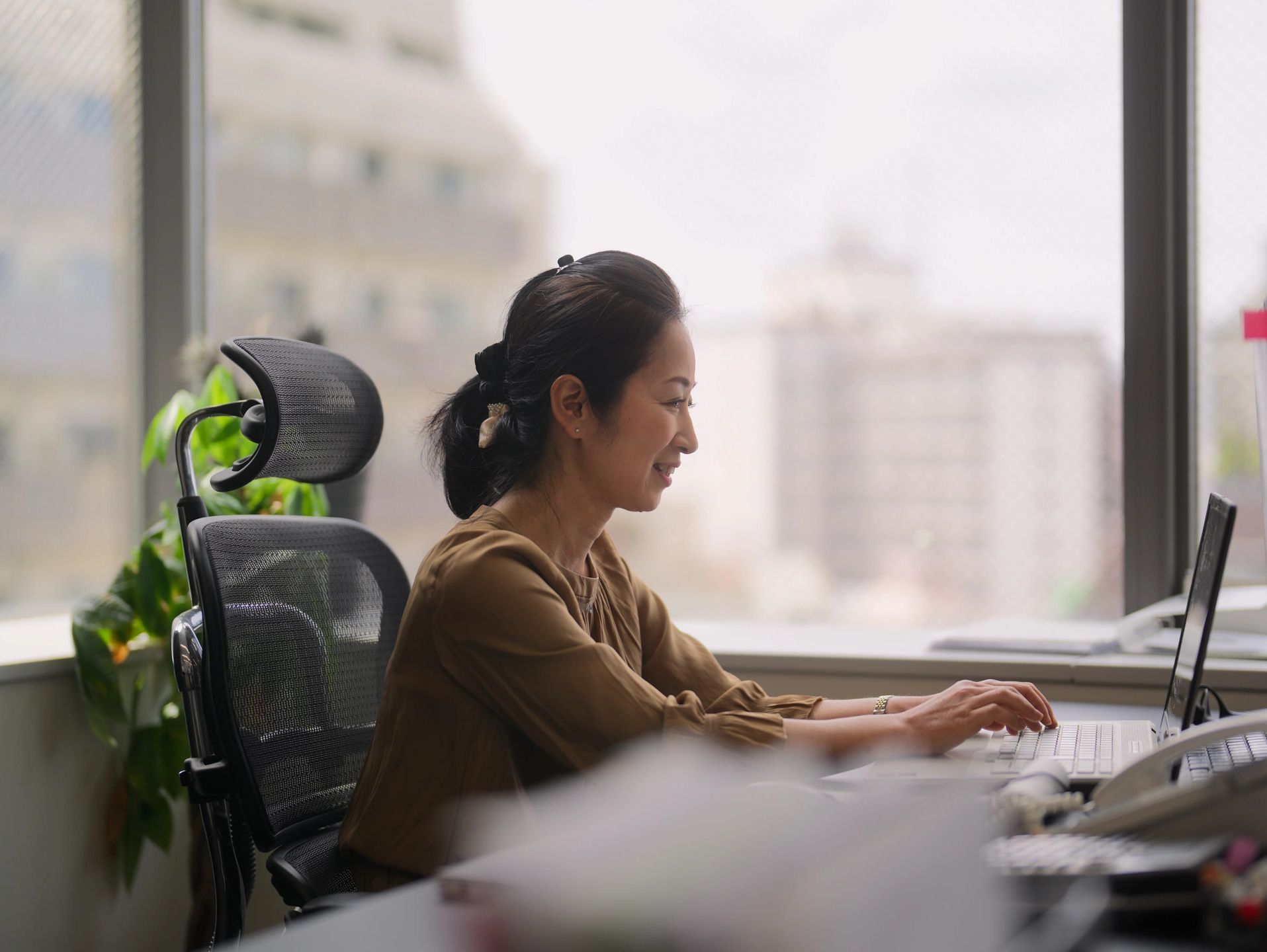 Woman working on a laptop in a modern office with large windows.