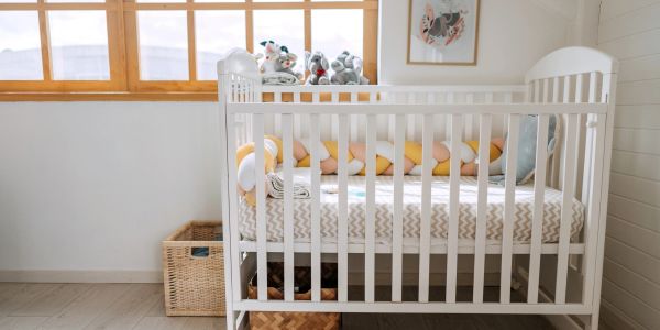 A white baby crib near a window with toys and cushions.
