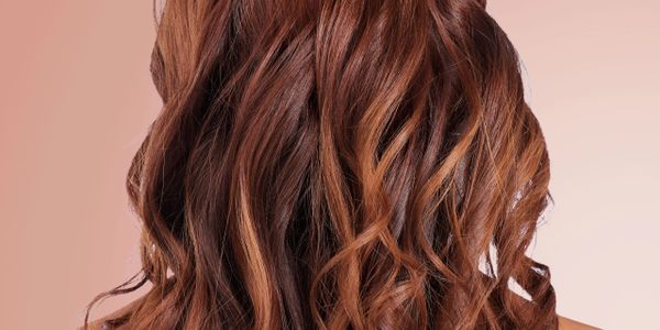 Close-up of wavy, chestnut brown hair with highlights against a peach background.