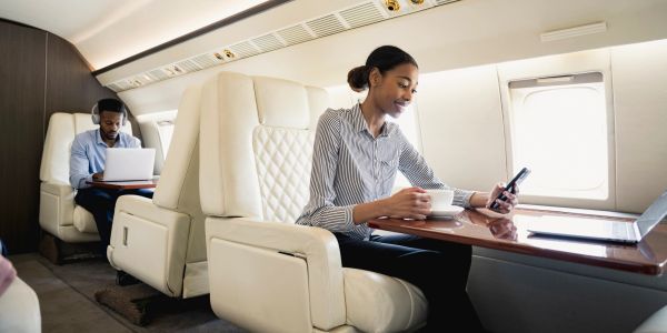 Woman using smartphone and drinking coffee on a private jet.