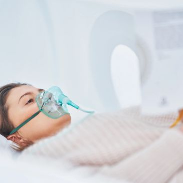 Patient lying in hospital bed with oxygen mask.