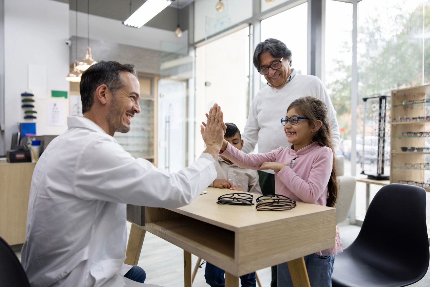 Optometrist high-fiving a young girl trying on glasses with her family.