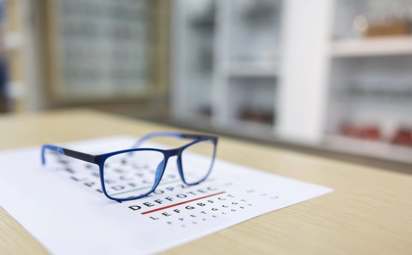 Blue eyeglasses on an eye chart on a wooden table.