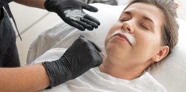 A woman receives a facial treatment with cream applied under her nose.