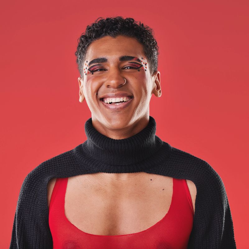LGBTQ, beauty portrait and black man isolated on red background for creative cosmetics, makeup and queer lifestyle. Young, edgy gen z model or gay person headshot for fashion and face art in studio