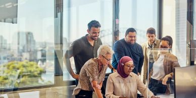 Team collaborates around a computer in a bright office.
