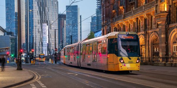 A modern tram moving through a city street at dusk.