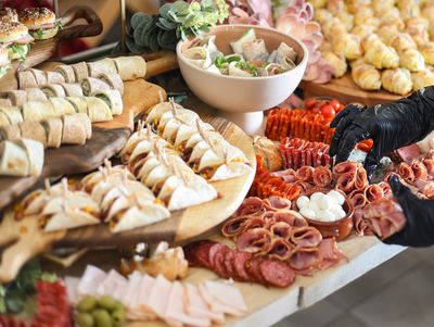 A charcuterie table with meats, cheeses, wraps, and appetizers being arranged.