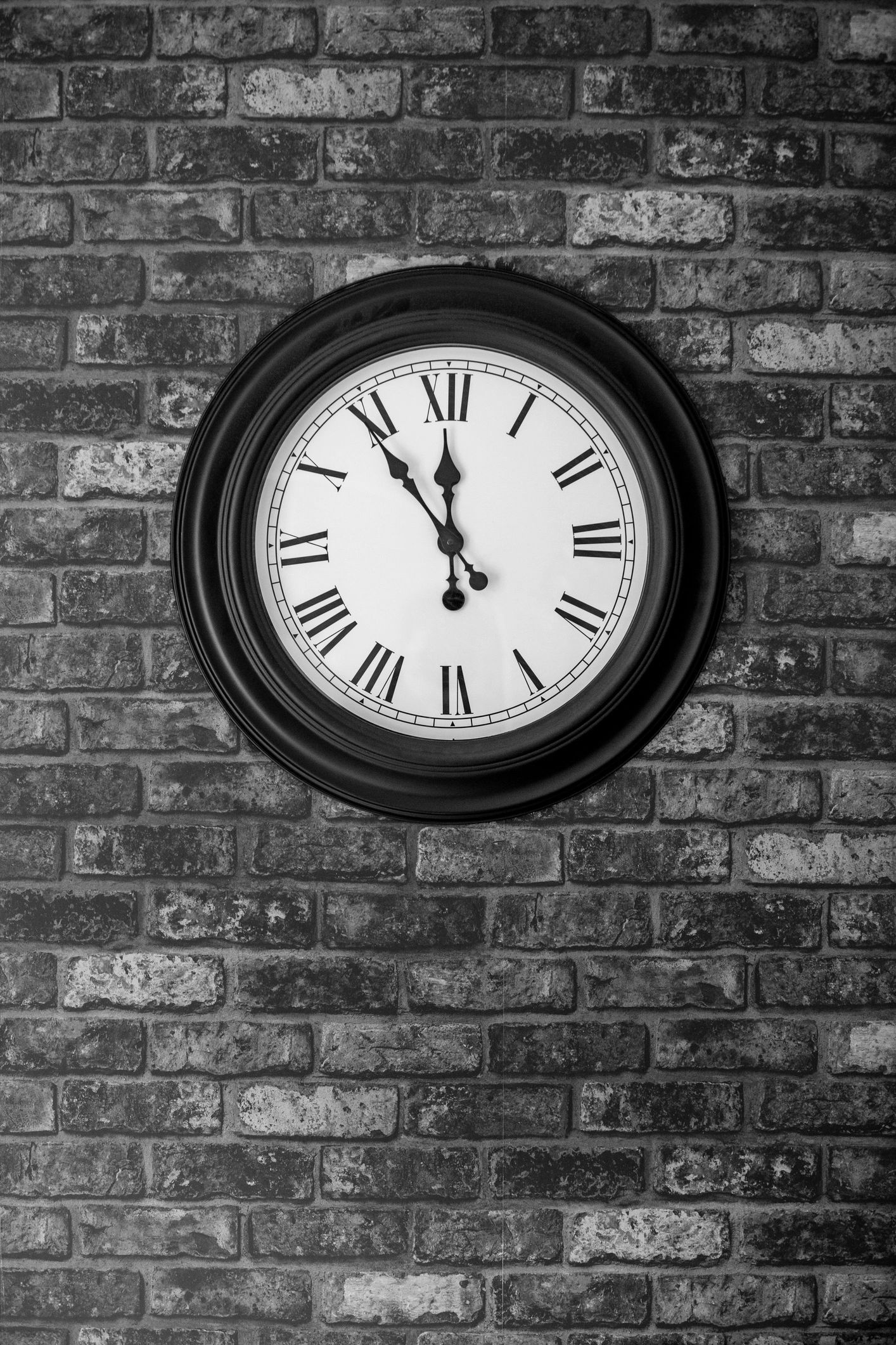 Classic clock on brick wall showing 11:55.