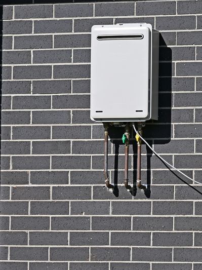 White tankless water heater mounted on a gray brick wall.