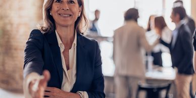 Smiling businesswoman extending hand for a handshake in an office setting.