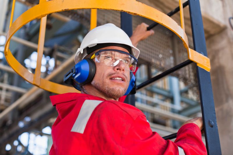 Worker climbing ladder at oil refinery