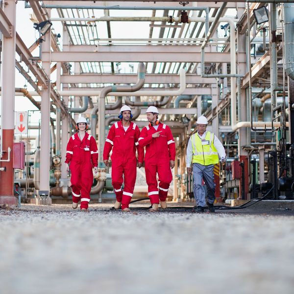 Four industrial workers walking in a plant wearing safety gear.