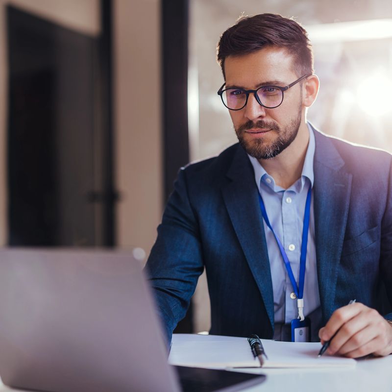 Young focused financier sitting at desk doing paperwork, working with bank taxes, loans, debits using laptop in office.