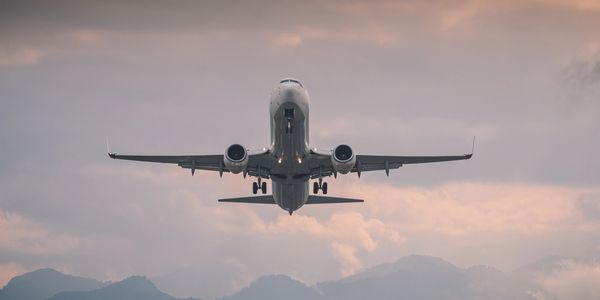 Airplane taking off against a cloudy sky and mountain backdrop.