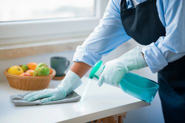 Person cleaning a kitchen counter with spray and cloth.