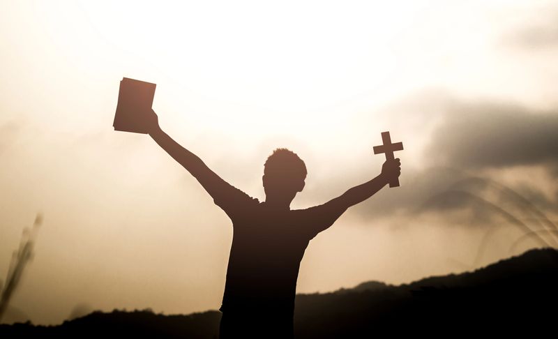 Human holding Holy Bible book and christian cross with light sunset background