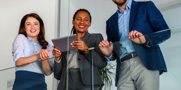 Three diverse business professionals smiling and standing on a balcony in an office setting.