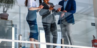 Three business professionals discussing work while standing by a glass railing.