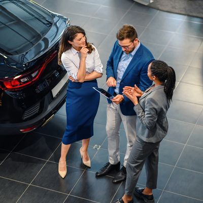 Three professionals discussing near a black car in a showroom.
