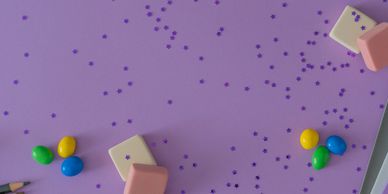 Colorful candies and pink erasers on a purple surface with scattered confetti.