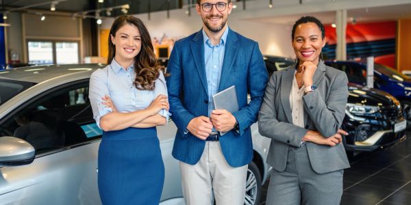 Three smiling car salespeople posing inside a dealership.