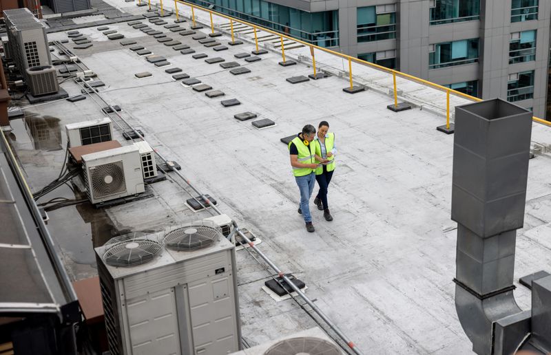 Team of maintenance engineers doing a routine inspection on the rooftop of a building and taking notes on his tablet computer