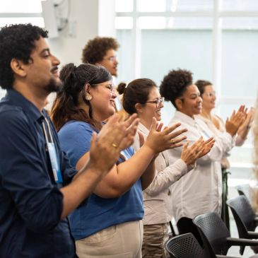 A diverse group of people enthusiastically applauding in a bright room.