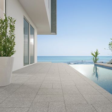 Modern patio with an infinity pool overlooking the ocean on a clear day.