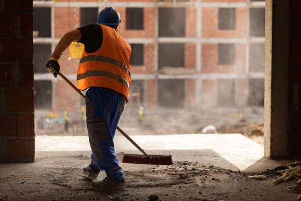 Construction worker sweeping debris inside an unfinished building.
