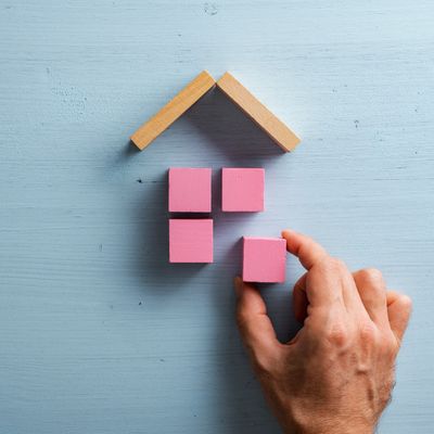 Hand arranging pink blocks to form a house shape with wooden roof pieces.