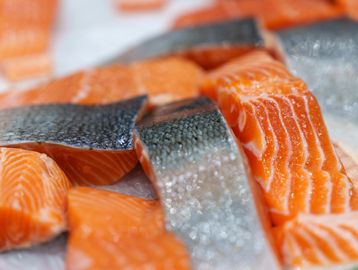 Fresh salmon fillets with skin on a white surface.