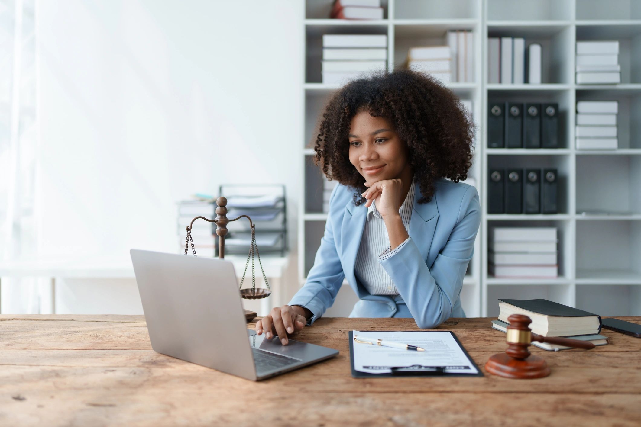 Woman lawyer working on a laptop in an office with legal books and a gavel.