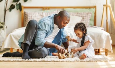 Father and daughter playing with wooden blocks on the floor.