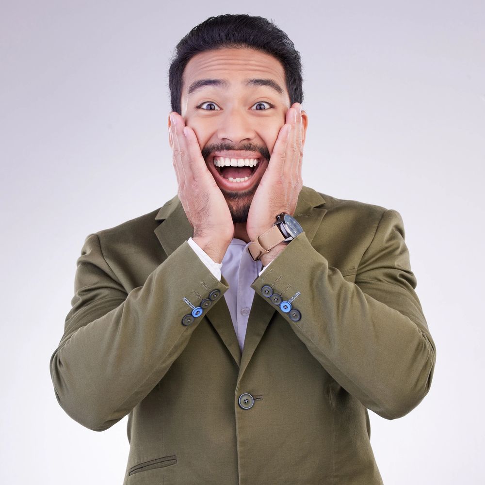 Excited man in olive blazer with hands on cheeks, expressing surprise and joy.