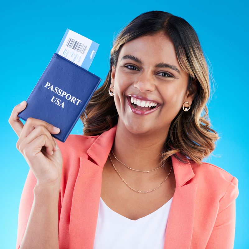 Passport, excited and woman portrait isolated on blue background for USA travel opportunity, immigration or holiday. Identity documents, flight ticket and happy face of young indian person in studio