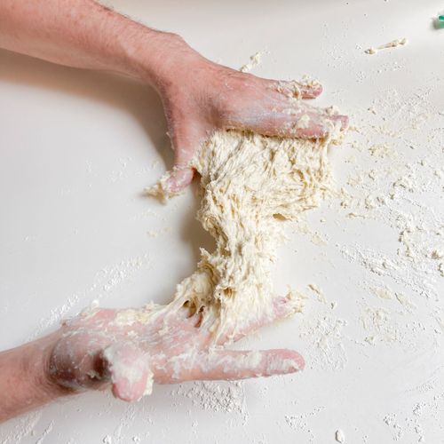 Hands kneading sticky dough on a floured surface.
