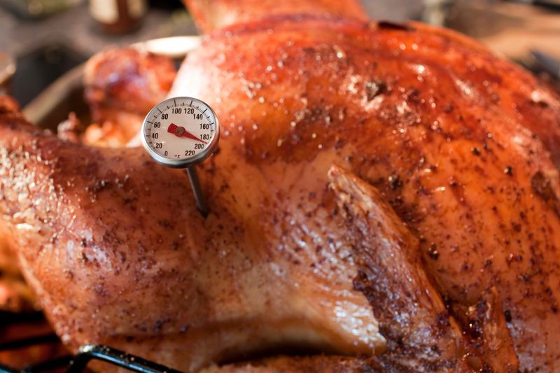 Roasted Turnkey fresh out of the oven. There is a little meat thermometer in the bird that reads 180 Roasted Turnkey fresh out of the oven. There is a little meat thermometer in the bird that reads 180?. The Fowl is Ready! This shot has a pretty narrow depth of field, focussing on the temperature gauge. The texture of the skin is fantastic and indicative of a perfectly cooked Thanksgiving turkey. The background has blurry kitchen elements in it.  - A great shot for preparation cookbooks, ingredient, catalogs, chef, diet and cooking websites or magazines  The bird is in a roasting Pan